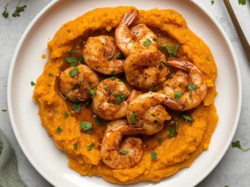 A vibrant dish of spicy Cajun shrimp served alongside creamy sweet potato mash.