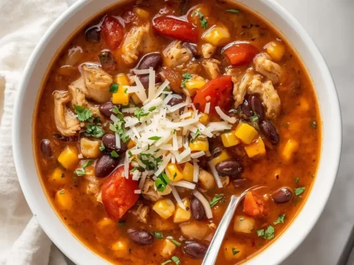 A steaming bowl of slow cooker chicken and black bean soup garnished with cilantro and lime wedges on a wooden table.
