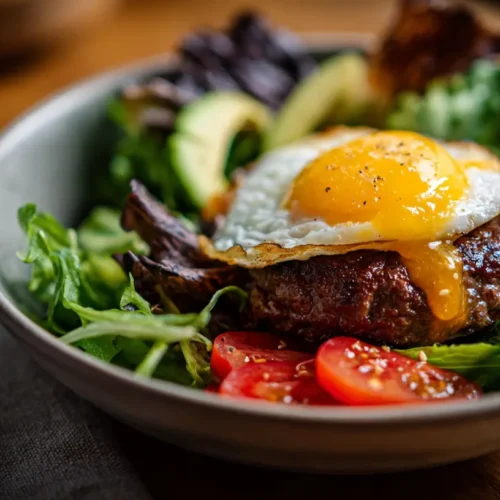A colorful loaded burger bowl featuring ground beef, crisp lettuce, tomatoes, and a variety of toppings served in a ceramic bowl.