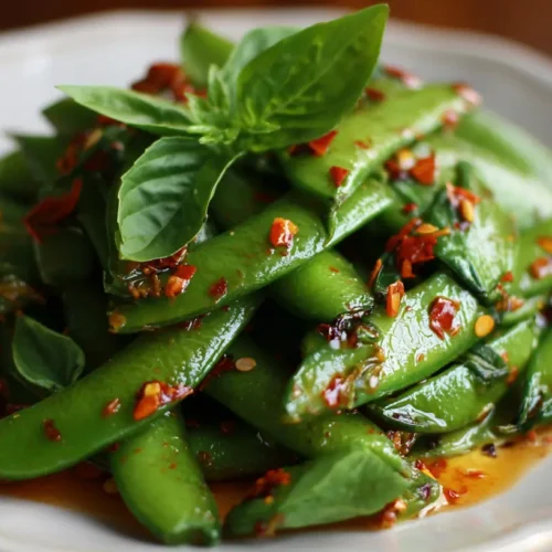 A fresh chili crisp snap pea salad in a white bowl with metal serving tongs.