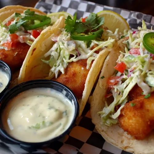 Two authentic Baja style fish tacos with fresh toppings and spicy sauce.