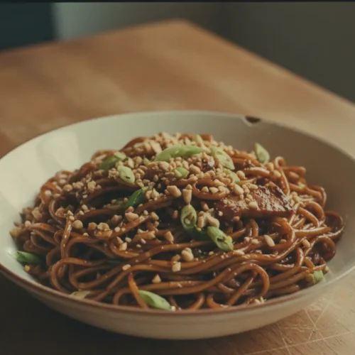 Close-up of hoisin garlic noodles in a bowl, garnished with green onions and sesame seeds.