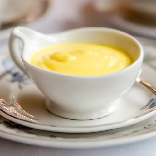 A serving bowl filled with smooth, yellow Hollandaise sauce.